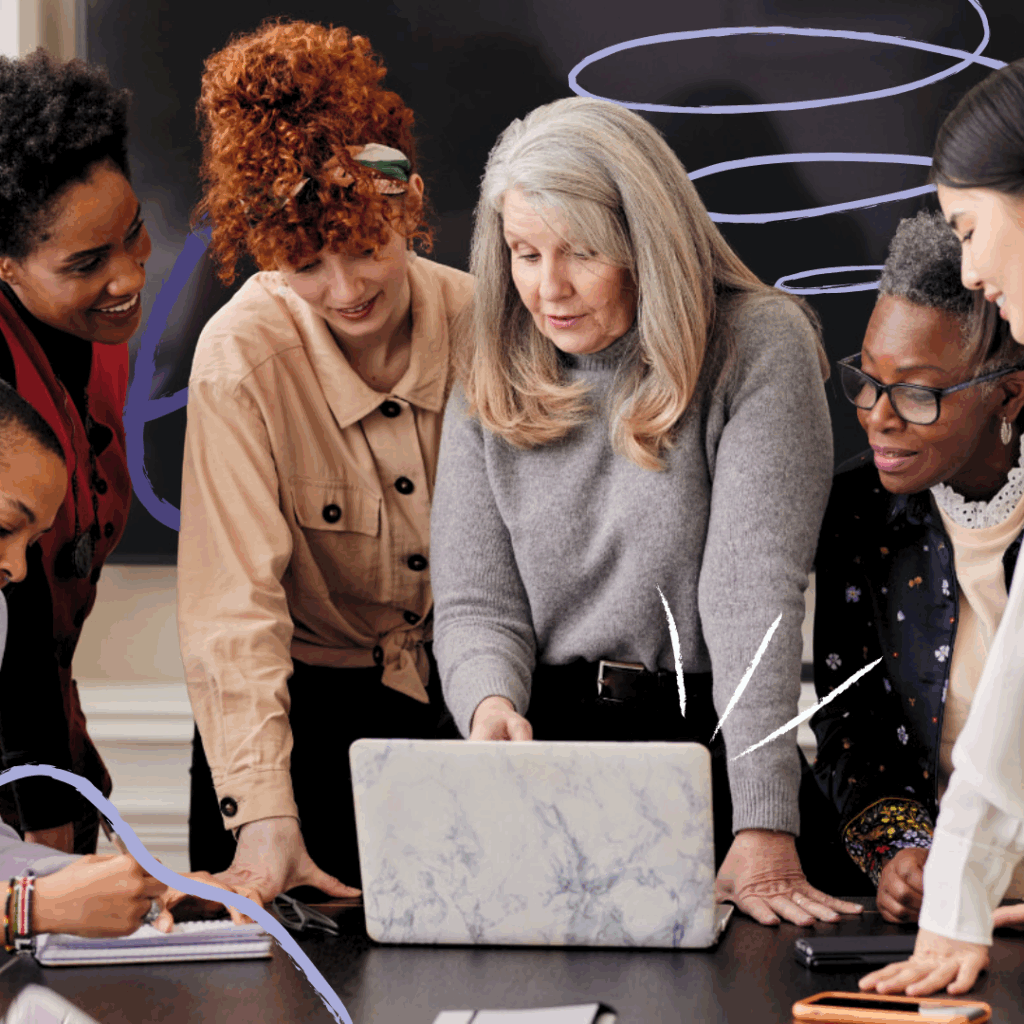 A woman points something out on a laptop to other women
